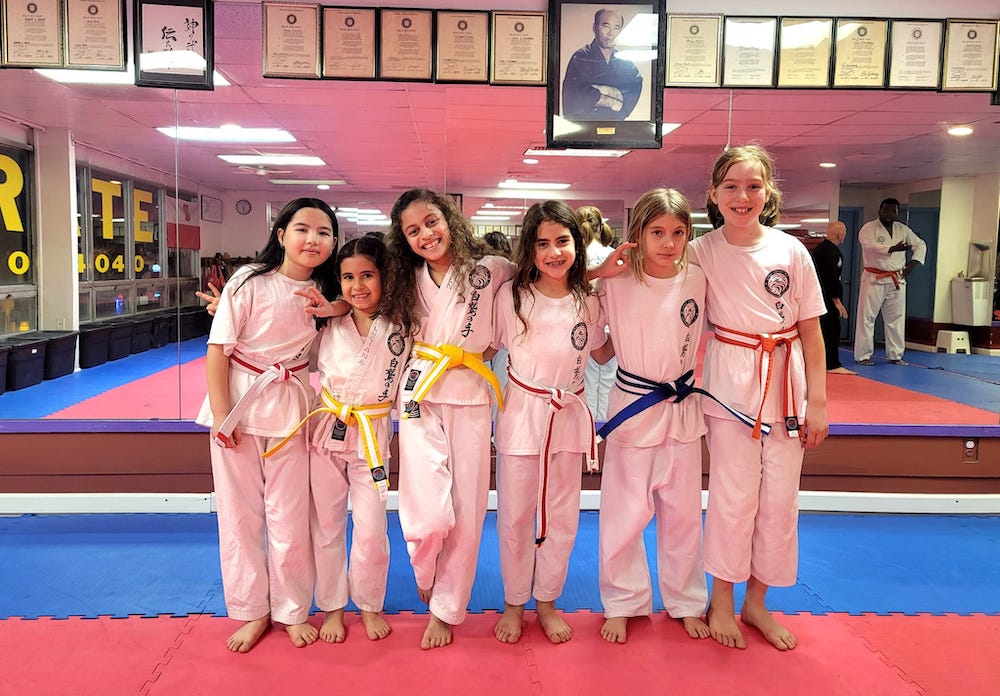 Group of children in karate uniforms at Polander Academy of Martial Arts in Bethesda, showcasing different belt colors, smiling and posing for a photo in a martial arts training environment.