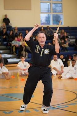 Martial arts instructor demonstrating advanced techniques with a wooden weapon during a black belt class at Polander Academy in Bethesda, surrounded by attentive students.