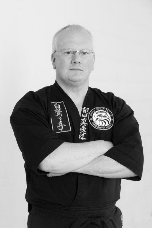 Instructor in black karate gi with arms crossed, representing Polander Academy of Martial Arts in Bethesda.