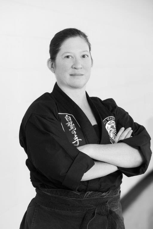 Instructor Helen Cawley in black martial arts gi with arms crossed, representing Polander Academy of Martial Arts in Bethesda.