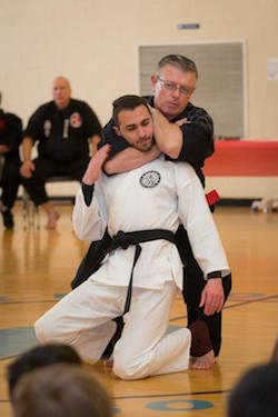 Martial arts demonstration at Polander Academy in Bethesda, featuring an instructor performing a technique on a student in a black belt class setting.