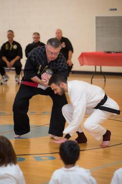 Martial arts demonstration at Polander Academy of Martial Arts in Bethesda, showcasing black belt training techniques with instructor guiding student in self-defense movements.